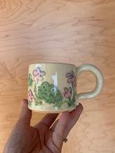 Load image into Gallery viewer, Hand holding a mug with frog design on a wooden surface
