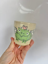 Load image into Gallery viewer, Hand holding a small ceramic cup with a green frog design on a white background
