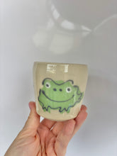 Load image into Gallery viewer, Ceramic cup with a green frog design held in a hand against a white background
